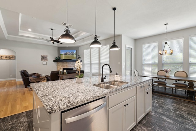 kitchen featuring a sink, white cabinetry, dishwasher, a stone fireplace, and an island with sink