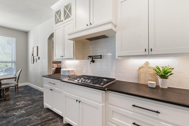kitchen featuring dark countertops, stainless steel gas cooktop, white cabinets, baseboards, and under cabinet range hood
