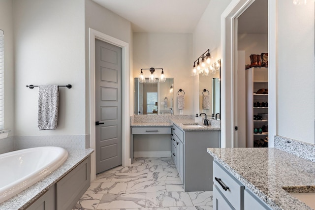 full bathroom featuring a garden tub, a sink, a spacious closet, marble finish floor, and two vanities