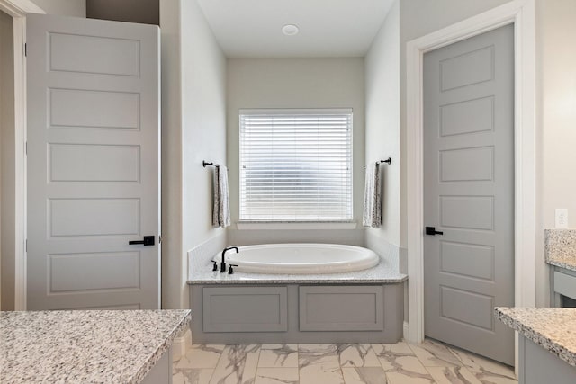 bathroom with a garden tub, marble finish floor, and vanity