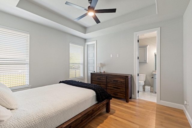 bedroom featuring light wood finished floors, baseboards, a ceiling fan, connected bathroom, and a raised ceiling