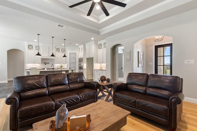 living area featuring arched walkways, baseboards, visible vents, a ceiling fan, and a raised ceiling