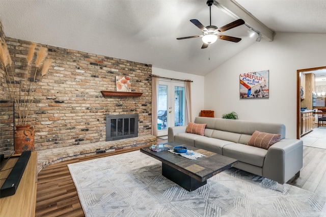 living area featuring a fireplace, brick wall, vaulted ceiling with beams, a ceiling fan, and light wood-style flooring