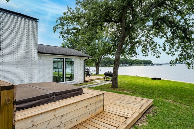 wooden terrace with a yard, a water view, and a covered hot tub