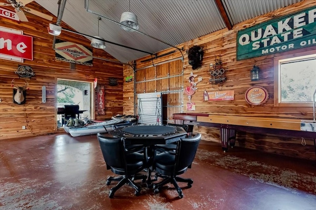 rec room featuring wooden walls, vaulted ceiling, finished concrete flooring, and a garage
