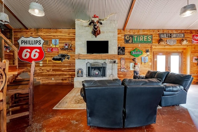 living area featuring concrete flooring, wooden walls, and a stone fireplace
