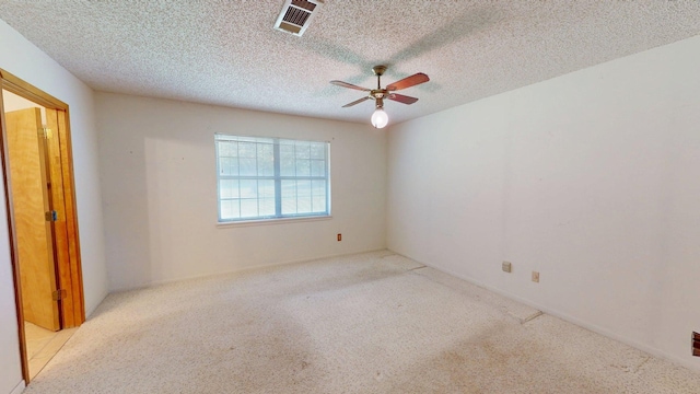 spare room with a textured ceiling, carpet flooring, visible vents, and a ceiling fan