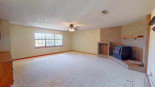 unfurnished living room featuring carpet flooring, a ceiling fan, a wood stove, and visible vents