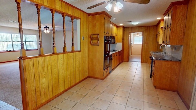 kitchen with a sink, a textured ceiling, brown cabinetry, wooden walls, and ceiling fan