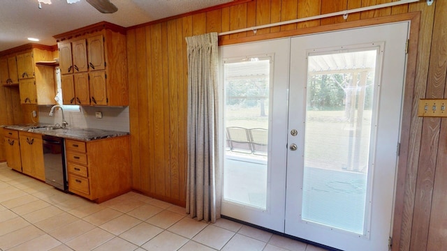 kitchen with french doors, a sink, dishwasher, brown cabinetry, and wooden walls