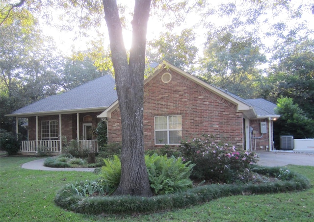 view of front of home with central AC unit, brick siding, a front lawn, and covered porch
