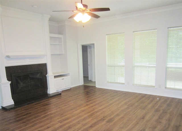 unfurnished living room with dark wood-style flooring, a fireplace with raised hearth, built in shelves, ceiling fan, and ornamental molding