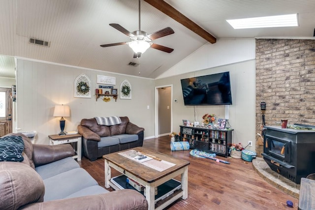 living area featuring lofted ceiling with beams, a wood stove, a ceiling fan, wood finished floors, and visible vents