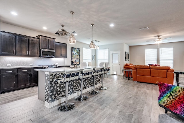 736 Wilmott Ter, Fort Worth, TX 76247 - kitchen with stainless steel microwave, a kitchen bar, a sink, light wood-style flooring, and a kitchen island with sink