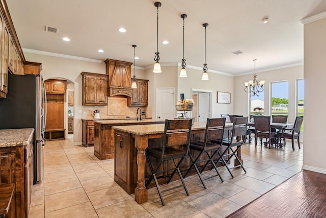 kitchen with a kitchen island with sink, arched walkways, freestanding refrigerator, backsplash, and light tile patterned floors