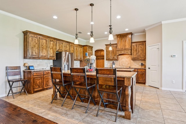 kitchen featuring backsplash, stainless steel fridge, brown cabinetry, and custom exhaust hood