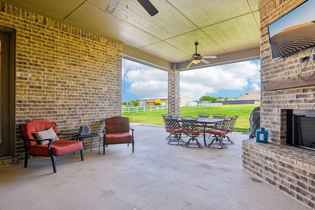 view of patio with a ceiling fan, an outdoor brick fireplace, outdoor dining area, and fence