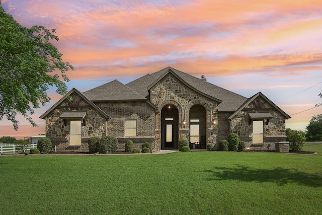 french country inspired facade featuring stone siding, roof with shingles, and a front yard
