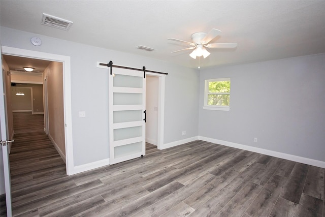 unfurnished bedroom with a barn door, baseboards, wood finished floors, and visible vents