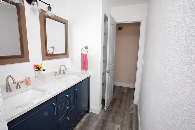 bathroom with baseboards, wood finished floors, a sink, and double vanity