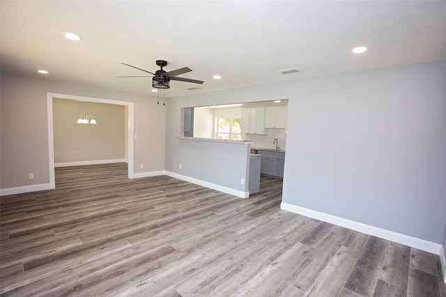 unfurnished living room with wood finished floors, visible vents, a sink, baseboards, and ceiling fan with notable chandelier