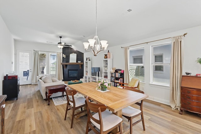 dining area with ceiling fan with notable chandelier, light wood-type flooring, a fireplace, lofted ceiling, and visible vents
