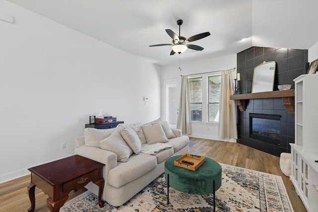 living area featuring a tile fireplace, lofted ceiling, wood finished floors, baseboards, and ceiling fan