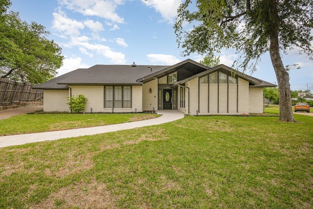 mid-century inspired home featuring fence, a shingled roof, brick siding, and a front yard