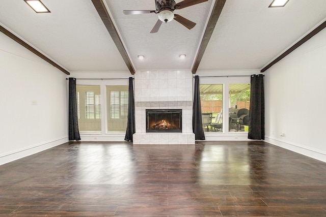 unfurnished living room featuring wood finished floors, lofted ceiling with beams, ceiling fan, a tiled fireplace, and baseboards