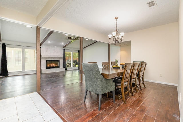 dining space with wood finished floors, visible vents, baseboards, a fireplace, and ceiling fan with notable chandelier