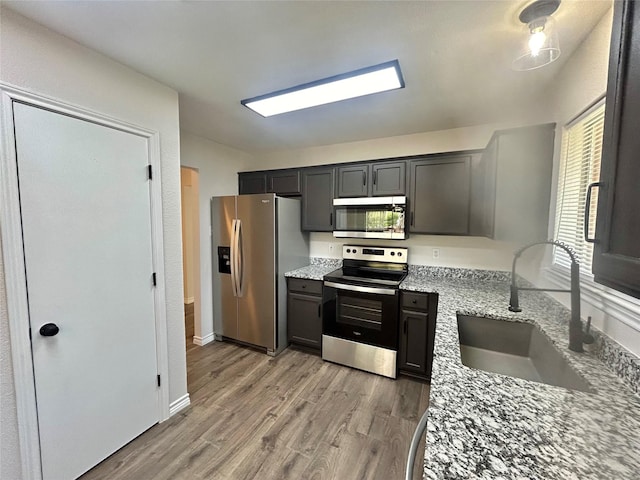 kitchen with light stone counters, light wood finished floors, stainless steel appliances, and a sink