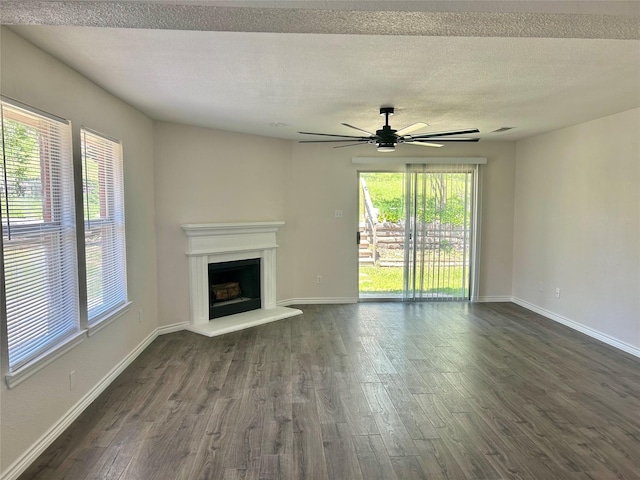 unfurnished living room with a fireplace with raised hearth, dark wood finished floors, a healthy amount of sunlight, and baseboards