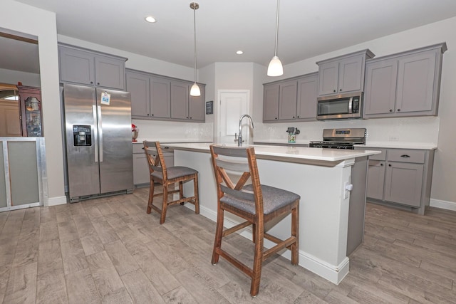 4125 Stockman Dr, Krum, TX 76249 - kitchen with appliances with stainless steel finishes, gray cabinetry, light wood-type flooring, light countertops, and an island with sink
