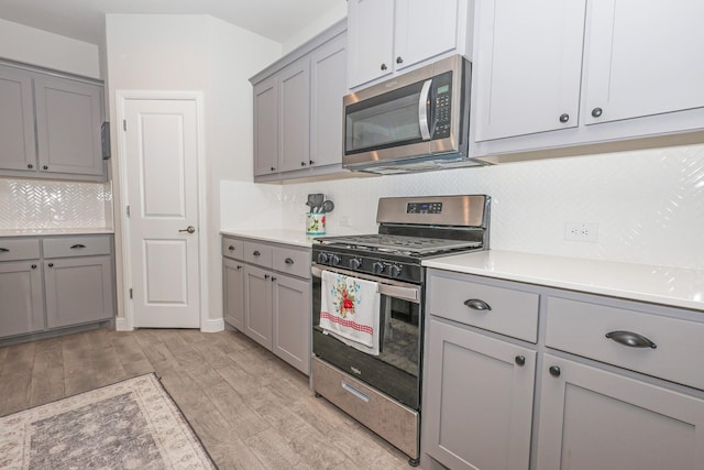 4125 Stockman Dr, Krum, TX 76249 - kitchen with stainless steel appliances, gray cabinets, decorative backsplash, light wood finished floors, and light countertops