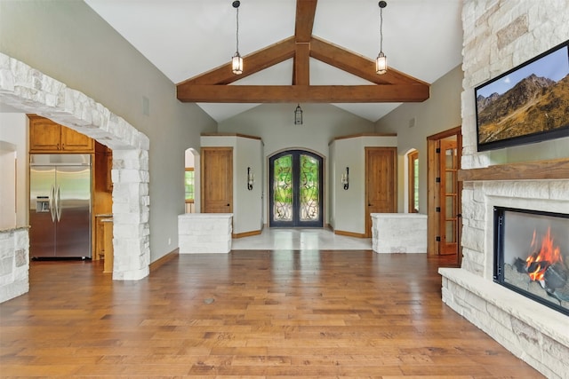 unfurnished living room with a stone fireplace, arched walkways, light wood-style flooring, and beam ceiling