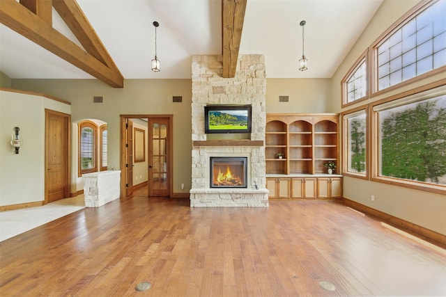 unfurnished living room featuring a stone fireplace, light wood finished floors, high vaulted ceiling, and beamed ceiling