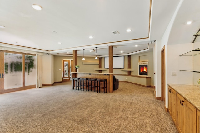 interior space with light colored carpet, baseboards, a kitchen breakfast bar, and a warm lit fireplace