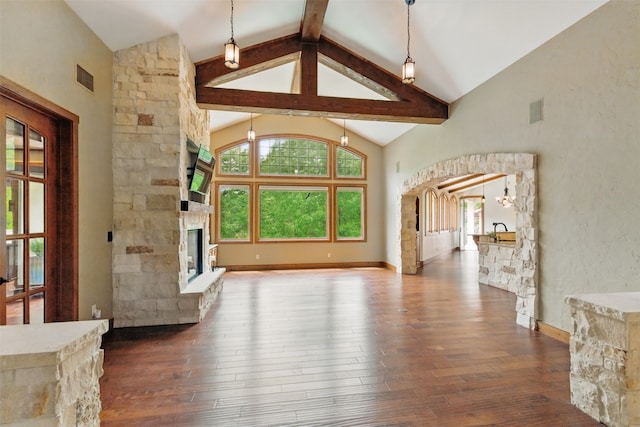 unfurnished living room featuring wood-type flooring, beamed ceiling, a stone fireplace, and plenty of natural light