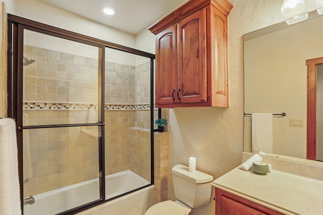 bathroom featuring toilet, a textured wall, bath / shower combo with glass door, and vanity