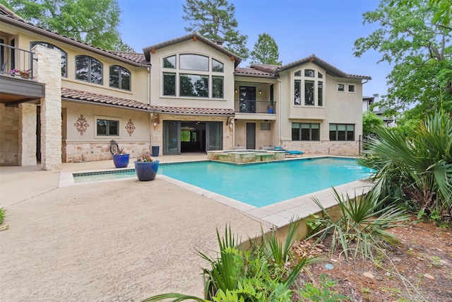 rear view of property with an in ground hot tub, stucco siding, a balcony, and stone siding