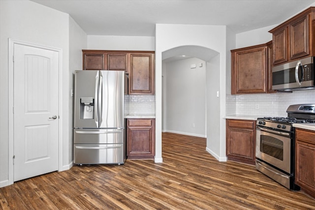 5208 Hidden Knolls Dr, Mckinney, TX 75071 - kitchen with appliances with stainless steel finishes, arched walkways, dark wood-type flooring, backsplash, and light countertops