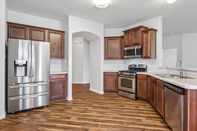 5208 Hidden Knolls Dr, Mckinney, TX 75071 - kitchen with appliances with stainless steel finishes, a sink, arched walkways, dark wood-type flooring, and decorative backsplash