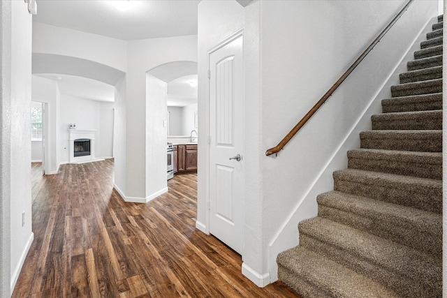 5208 Hidden Knolls Dr, Mckinney, TX 75071 - hallway featuring dark wood-style floors, arched walkways, stairs, a sink, and baseboards