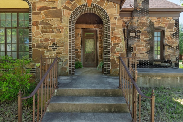 entrance to property with brick siding, roof with shingles, and stone siding