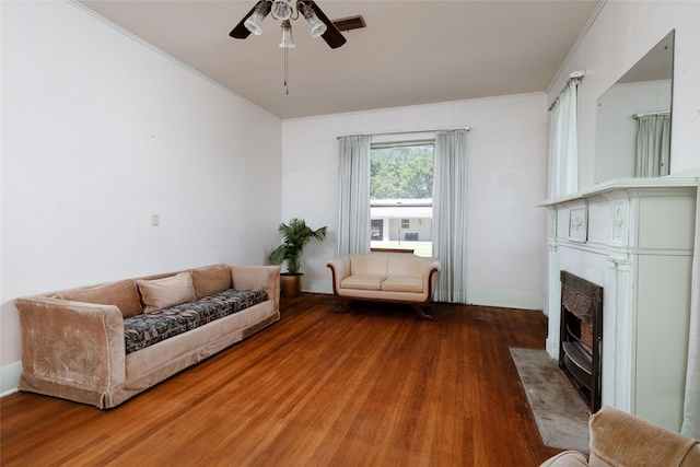 living area with a fireplace with flush hearth, wood finished floors, ornamental molding, and ceiling fan