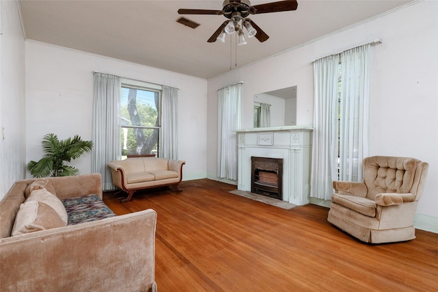 living room with a fireplace with flush hearth, ceiling fan, crown molding, and wood finished floors