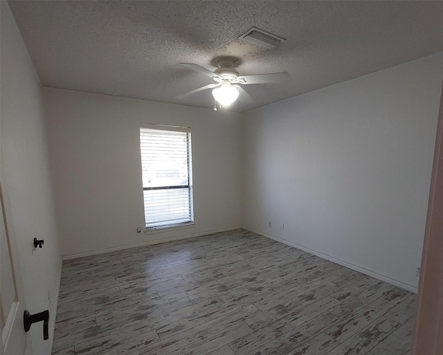 empty room featuring wood finished floors, a textured ceiling, ceiling fan, baseboards, and visible vents