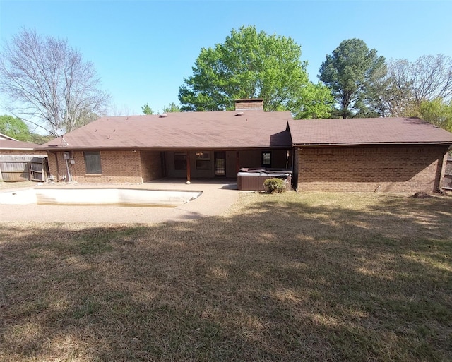 back of house featuring a chimney, a yard, a patio, brick siding, and a hot tub