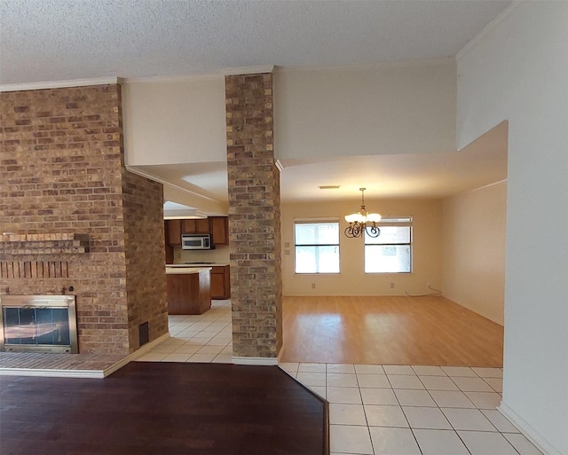unfurnished living room with light tile patterned floors, a fireplace, an inviting chandelier, and decorative columns