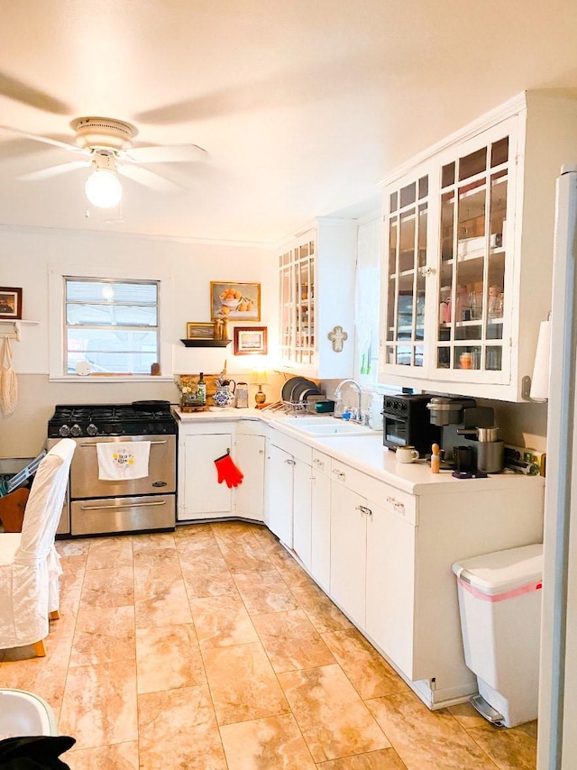 kitchen with stainless steel gas stove, light countertops, a sink, glass insert cabinets, and white cabinetry
